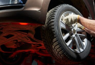 The hands of a caucasian auto mechanic take off, dismantle, hang up a car wheel holding the spokes of an alloy wheel. the car is raised on a lift, you can see the bottom The hands of a caucasian auto mechanic take off, dismantle, hang up a car wheel holding the spokes of an alloy wheel. the car is raised on a lift, you can see the bottom. High quality photo